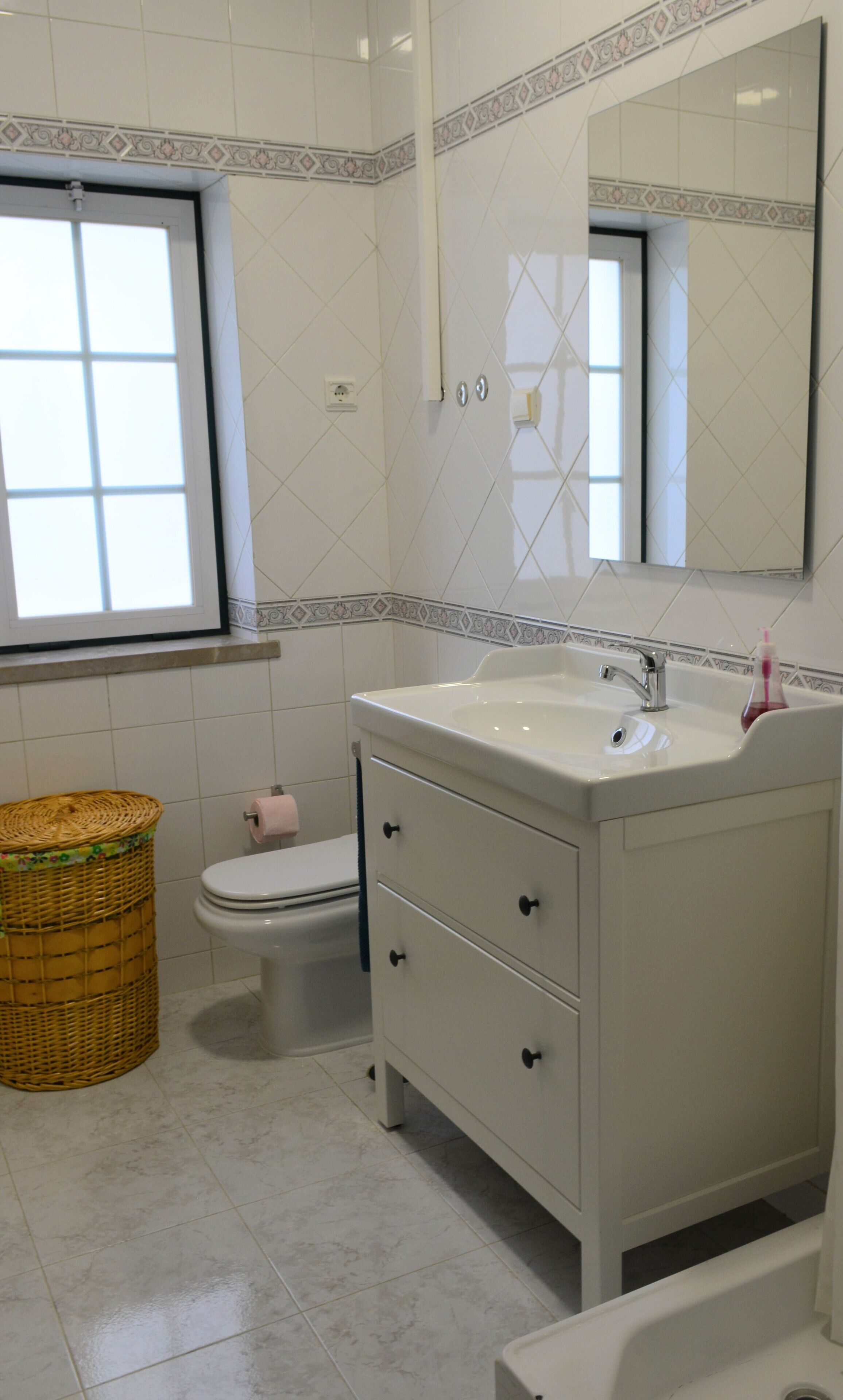 A bathroom with a white sink, a mirror, a toilet, and a wicker basket.