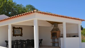 A covered outdoor area with a brick oven, white pillars, and plastic chairs. - Casal dos Cantos Poente (Quinta do Anjo)