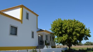 A white building with yellow trim and a tree in front. - Casal dos Cantos Poente (Quinta do Anjo)