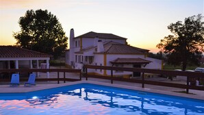 A swimming pool with a wooden deck and lounge chairs, surrounded by a fence. - Casal dos Cantos Poente (Quinta do Anjo)