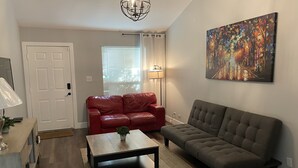 Un salon avec un canapé en cuir rouge, un canapé gris, une table basse et un tableau accroché au mur.