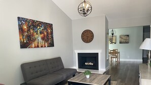 Un salon avec un canapé gris, une table basse, une cheminée et un grand tableau.