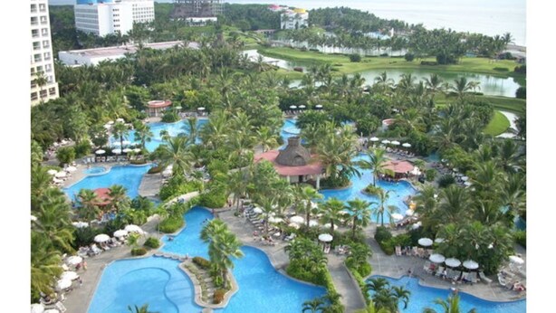 Un resort con varias piscinas rodeado de palmeras y un campo de golf al fondo.