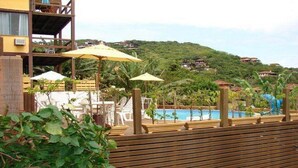 Zona de piscina con sombrillas, sillas de descanso y vistas a una colina con casas.