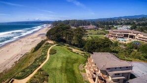 Vista aérea de una propiedad costera con playa, campo de golf y un edificio de resort.