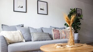 A modern living room with a grey sofa, multiple cushions, a wooden coffee table with decorative items, and framed pictures on the wall.