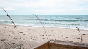 A beach with a wooden bench and tall grasses in the foreground.