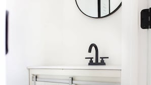 A white cabinet with a black faucet and a round mirror above it. There are two wicker baskets inside the cabinet.