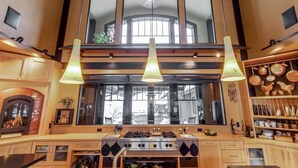 Una cocina con una estufa grande, luces colgantes y vistas al exterior a través de amplios ventanales.