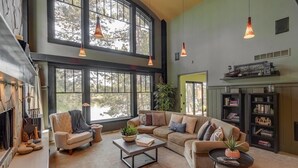 Amplia sala de estar con un sofá seccional grande, una mesa de centro y una chimenea. Cuenta con ventanas amplias que dejan entrar luz natural y ofrecen vistas al exterior.