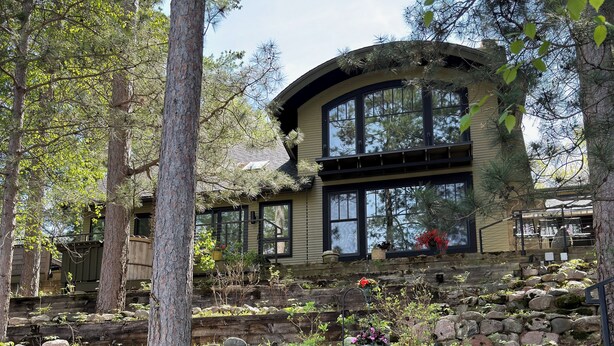 Una casa con una escalera de piedra que conduce a una terraza de madera, rodeada de árboles.
