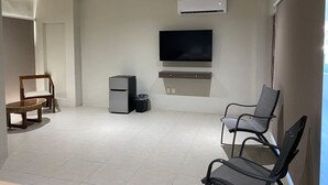 Ein modernes Wohnzimmer mit Flachbildfernseher, Deckenventilator und kleinem Kühlschrank.