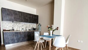 Een moderne keuken met donkere kastjes, een betegelde spatwand, en een eethoek met een blauwe tafel en witte stoelen.
