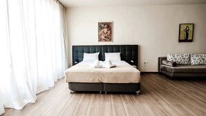Een hotelkamer met een groot bed, een slaapbank en twee schilderijen aan de muur.