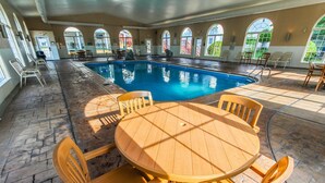 A pool area with a round wooden table and chairs, surrounded by arched windows and a tiled floor. - NEW! Christmas week in Branson 2 BR/3 BA/sleeps 8, indoor pool, 1486 sq ft (Branson)