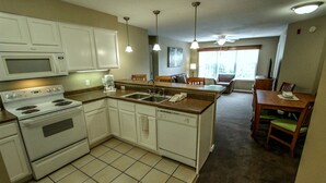 A compact kitchen with white cabinets, a microwave, stove, and a coffee maker. There is a dining area with a wooden table and chairs. - NEW! Christmas week in Branson 2 BR/3 BA/sleeps 8, indoor pool, 1486 sq ft (Branson)