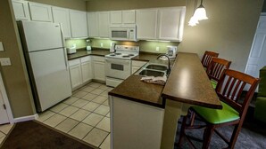 A compact kitchen with white cabinets, a microwave, stove, and a dining area with wooden chairs and a green cushioned bench. - NEW! Christmas week in Branson 2 BR/3 BA/sleeps 8, indoor pool, 1486 sq ft (Branson)