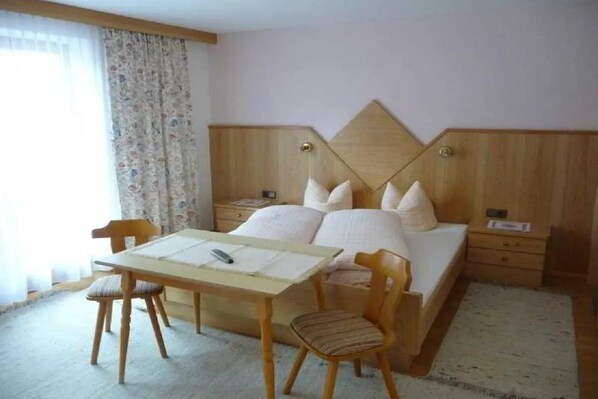 Un dormitorio con cama, una mesita de noche de madera, un escritorio con silla y una ventana con cortinas.