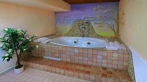 A bathroom with a large bathtub, a potted plant, and a mural on the wall. - Alpenheim Joergele (Soelden)