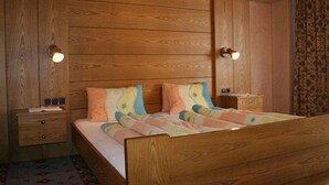 A wooden-paneled bedroom with a bed, two bedside tables, and a nightstand. - Alpenheim Joergele (Soelden)