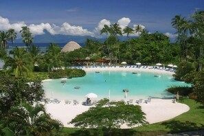 A resort pool with a white sandy beach, surrounded by lush greenery and palm trees. - Tahiti Ia Ora Beach Resort (Punaauia)