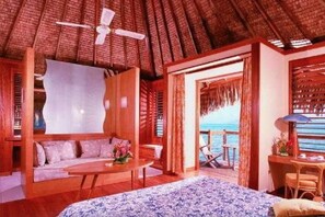 A room with a thatched roof, wooden furniture, a bed with a patterned bedspread, and a view of the sea. - Tahiti Ia Ora Beach Resort (Punaauia)