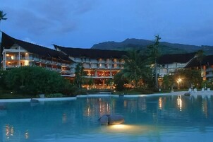 Un hotel de varios pisos, con piscina y montañas al fondo.