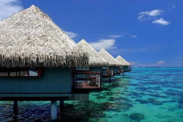 Overwater bungalows with thatched roofs and wooden walkways extending into clear turquoise water. - Tahiti Ia Ora Beach Resort (Punaauia)
