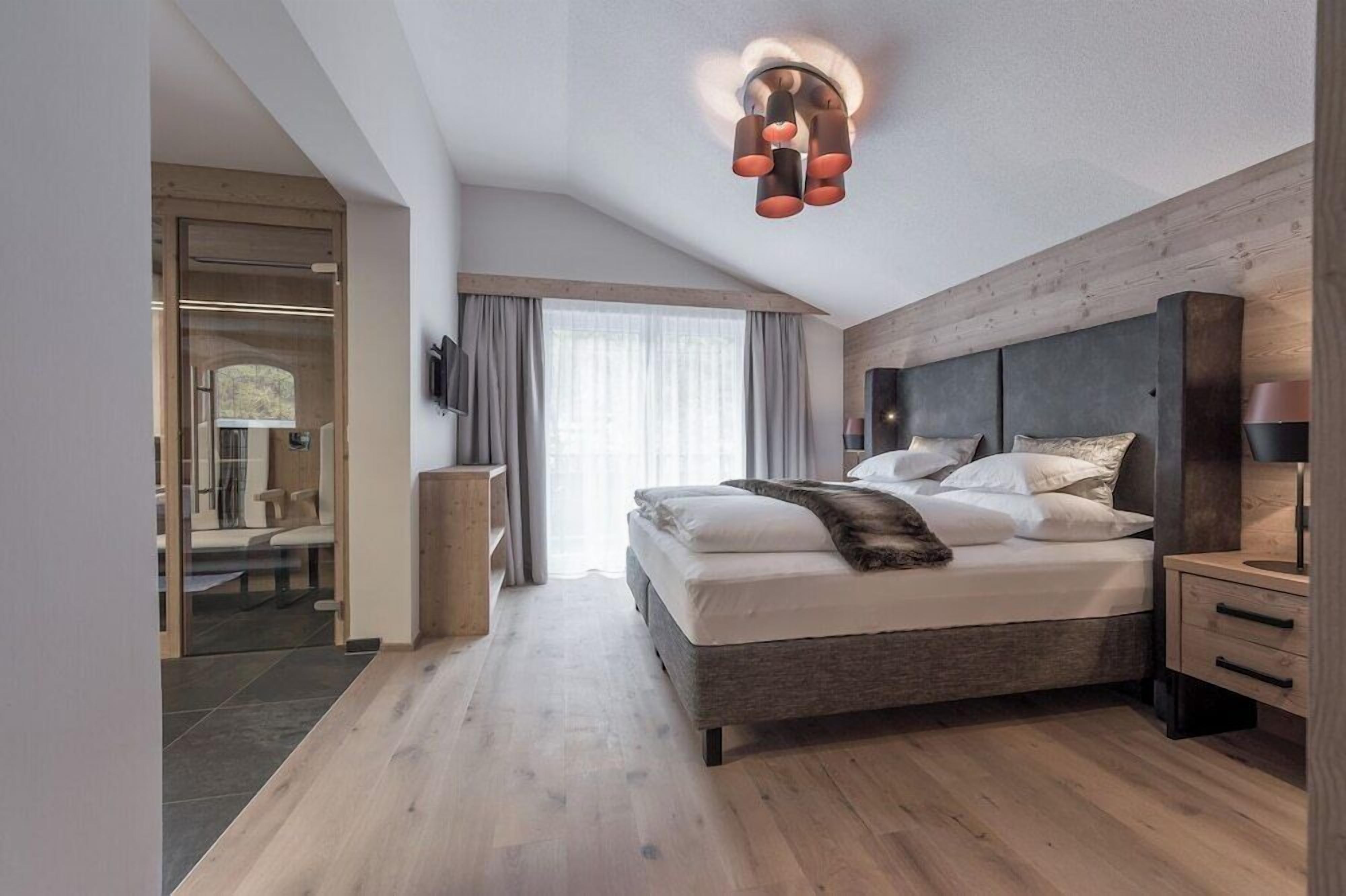 Ein modernes Schlafzimmer mit einem großen Bett, einem Nachttisch, einem an der Wand montierten Fernseher und einer Holzbalkendecke.