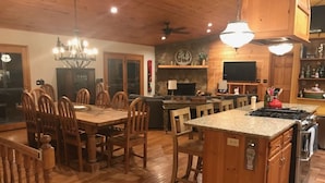 A spacious kitchen with wooden cabinetry, a central island, and a dining area with wooden chairs. - Lakefront Gem, Mtn views, dock + HOT TUB (Blairsville)