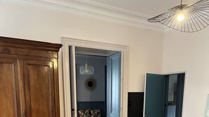 A dining area with a wooden table, six chairs, a large wooden cabinet, and a doorway leading to a room with a patterned floor. - Maison St Romain (Blaye)