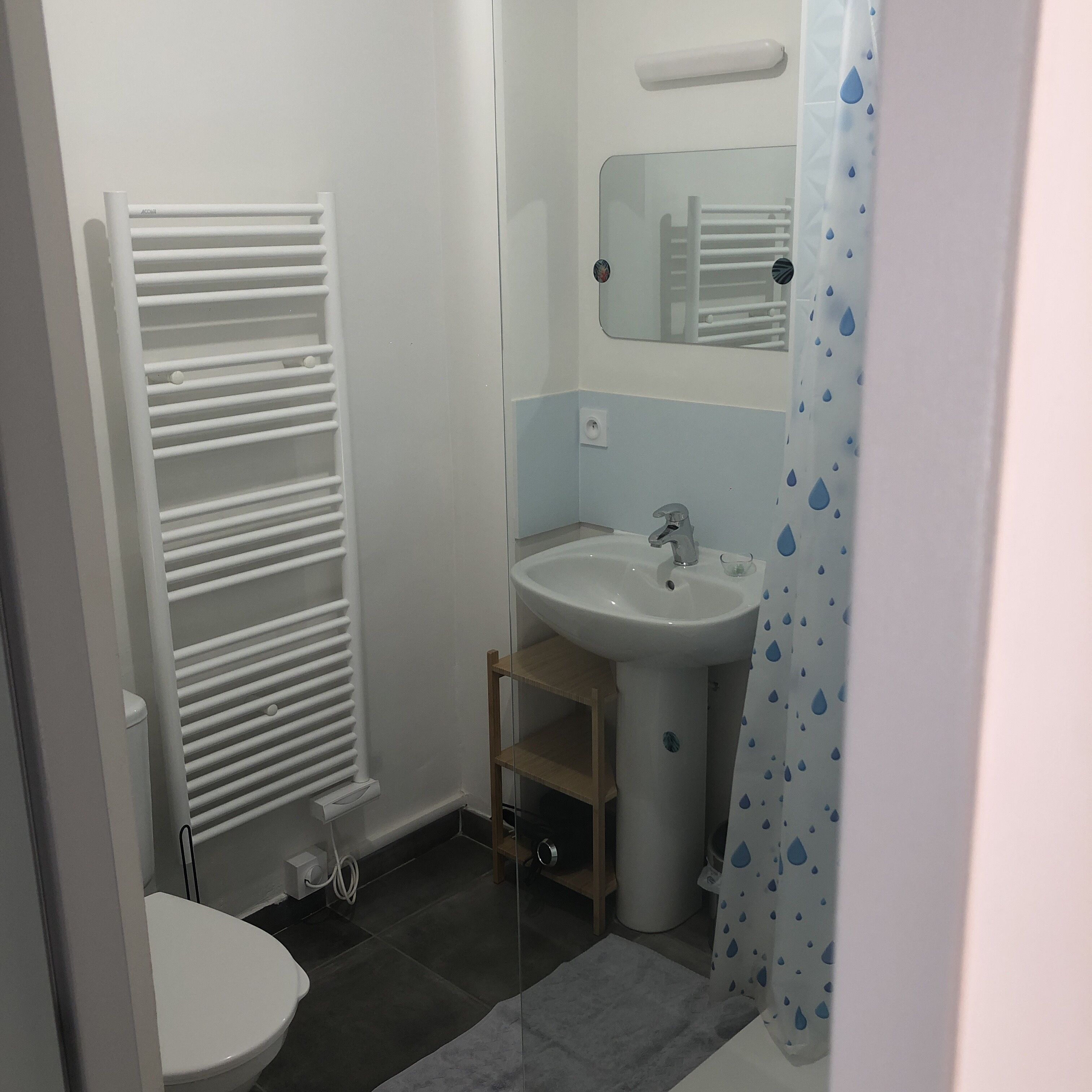 A small, modern bathroom with a toilet, a white sink, a mirror, and a towel rack.