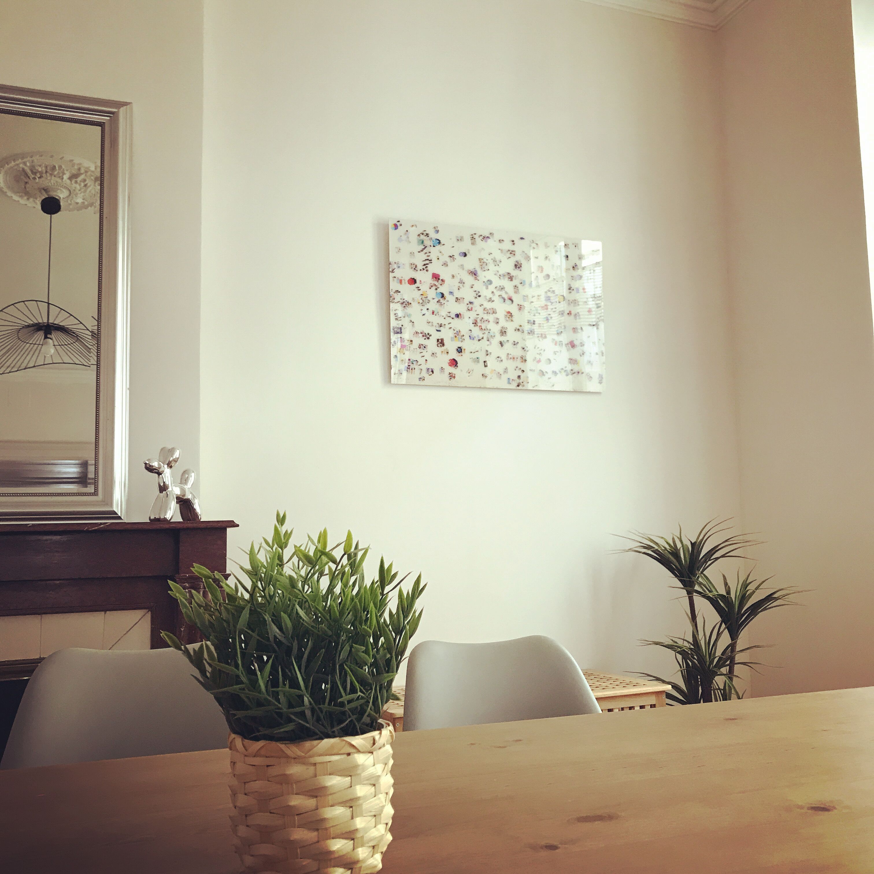 Un coin repas comprenant une table en bois, des chaises, un pot de fleurs en osier et une œuvre d’art accrochée au mur.
