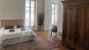 A bedroom with a bed, a wooden wardrobe, a window, and a plant. - Maison St Romain (Blaye)