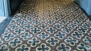 A hallway with patterned floor tiles, a bench with colorful cushions, and a door with stained glass panels. - Maison St Romain (Blaye)
