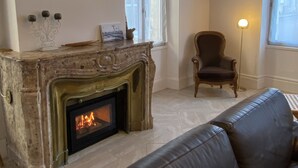 A living room with a fireplace, a leather sofa, a chair, and a lamp. - Maison St Romain (Blaye)