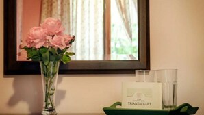 A vase with pink flowers on a table, a framed mirror, and a tray with a bottle and glasses. - Triantafillies Hotel (Volos)