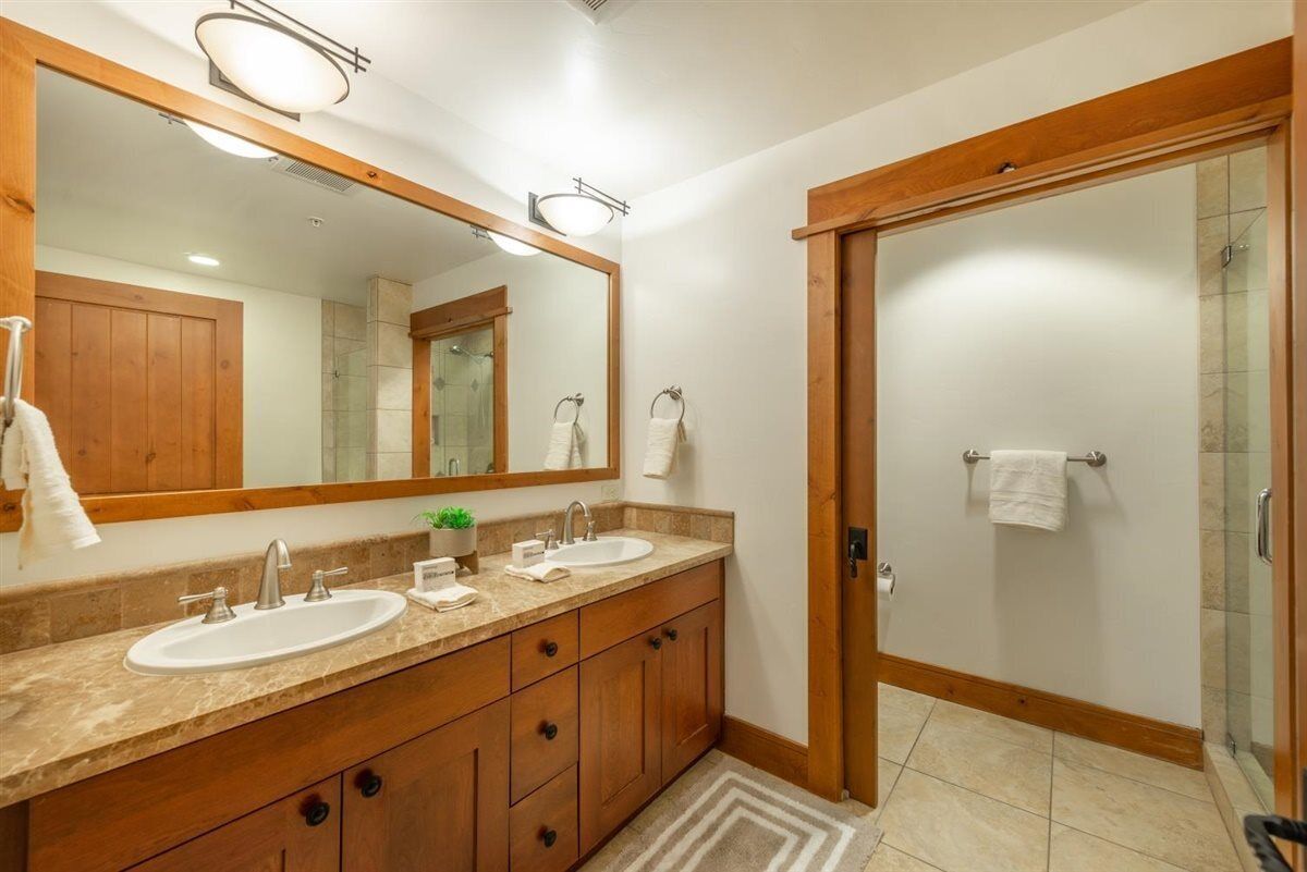 Une salle de bain avec deux lavabos, un grand miroir, des meubles en bois et une cabine de douche en verre.
