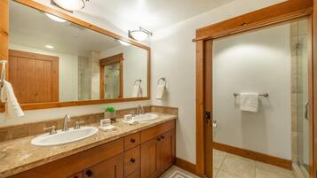 Une salle de bain avec deux lavabos, un grand miroir, des meubles en bois et une cabine de douche en verre.