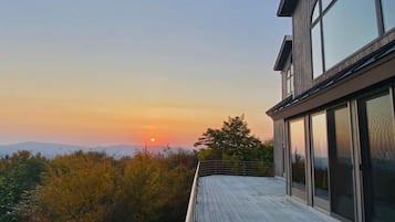 A modern building with large windows and a deck overlooking a scenic sunset view.
