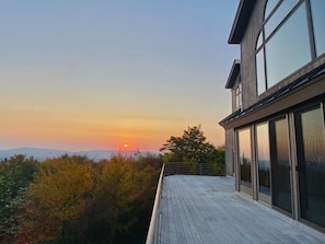 Een modern gebouw met grote ramen en een terras met uitzicht op een schilderachtige zonsondergang.