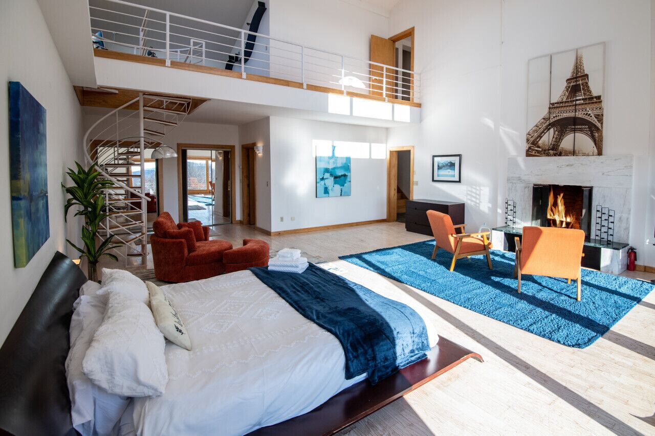 A spacious room with a large bed, a fireplace, a staircase, and a view of the Eiffel Tower.