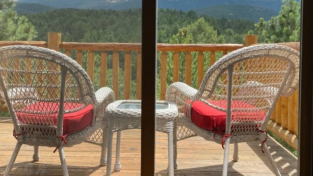 Two wicker chairs with red cushions on a wooden deck with a view of mountains. - Mountain Sunrise Cabin with breathe taking views. (Divide,)
