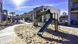 A modern outdoor area with a playground, including a slide, surrounded by buildings with balconies and a clear sky.