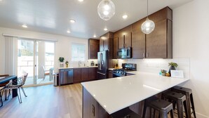 A modern kitchen with dark wood cabinets, stainless steel appliances, and pendant lighting.