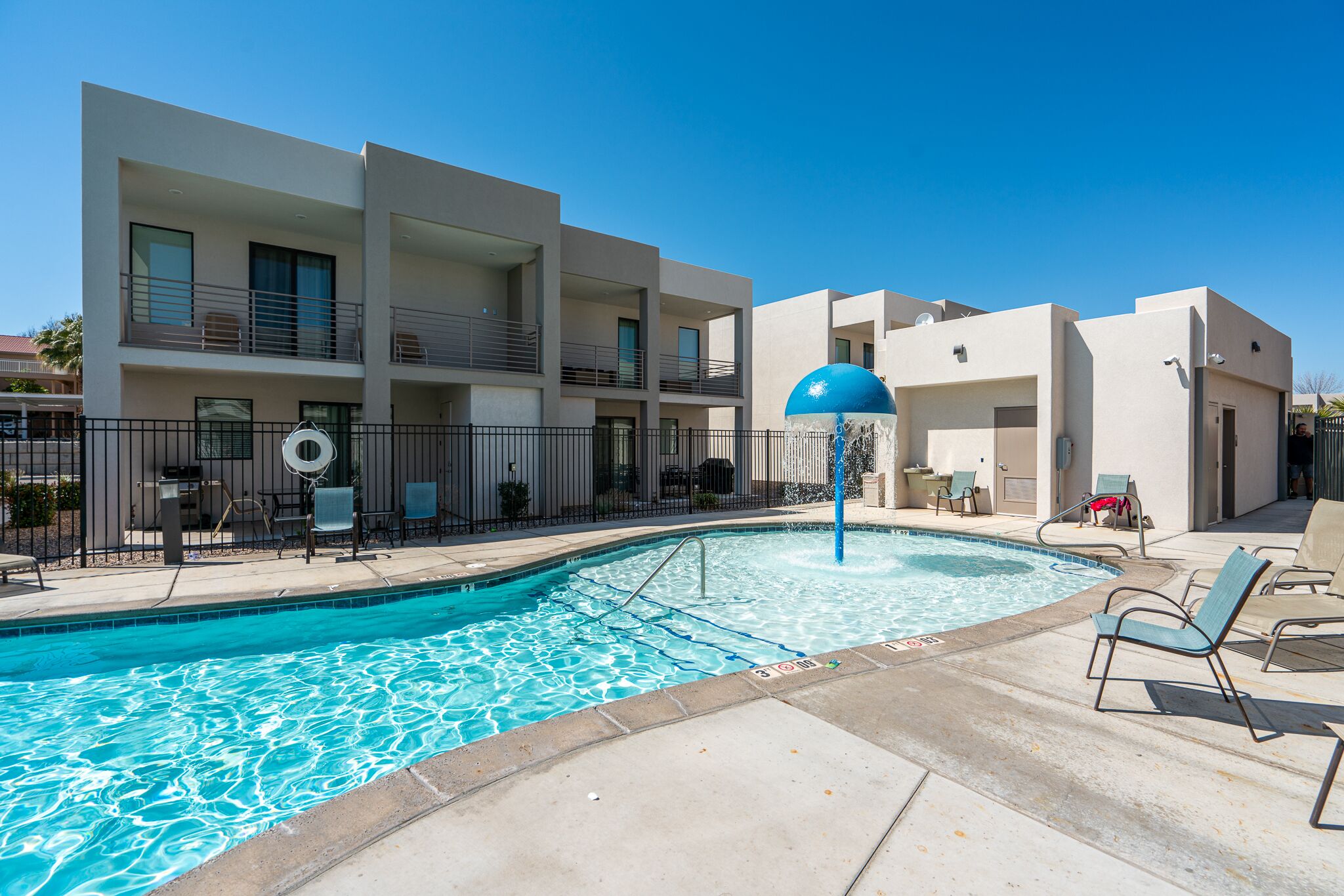 A swimming pool with lounge chairs and a blue umbrella, surrounded by a modern building with balconies.