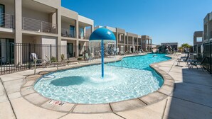 A pool area with a water feature, lounge chairs, and a building with balconies.