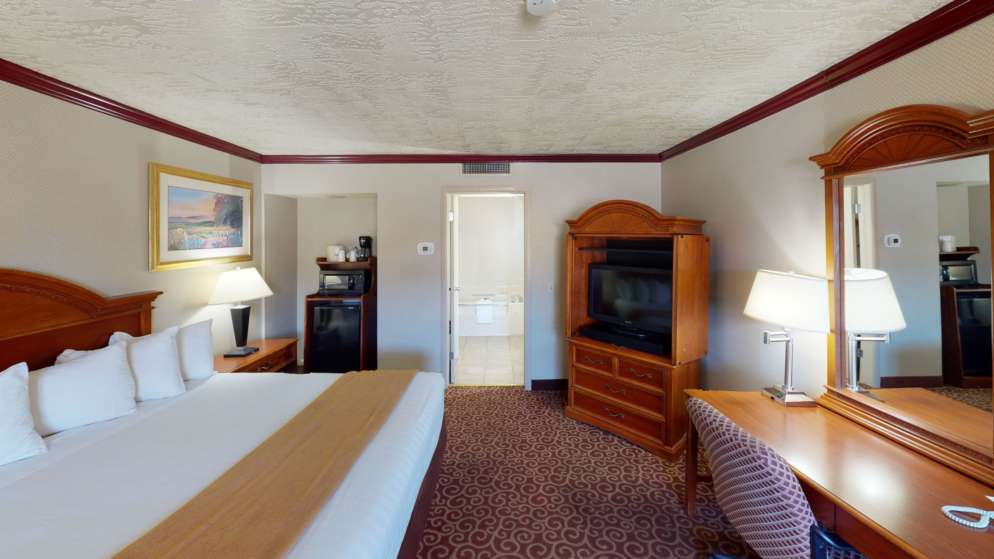 A hotel room with a large bed, a desk with a computer, a TV, and a mirror.