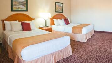 Une chambre d’hôtel avec deux lits, chacun doté d’une tête de lit en bois, de draps blancs et d’une couvre-lit marron. Il y a deux tables de chevet avec des lampes, et la chambre est recouverte d’un tapis à motifs.