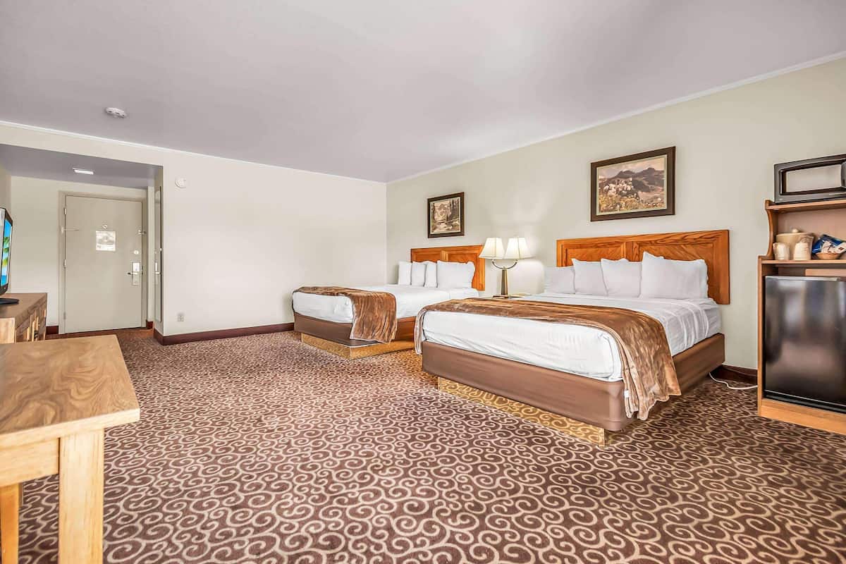 A hotel room with two beds, a desk, a television, and a door.